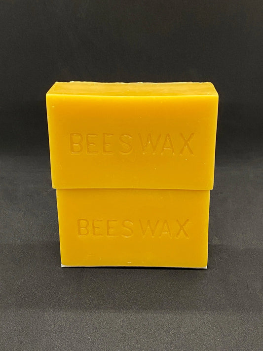 Two yellow beeswax blocks stamped BEESWAX stacked on top of each other on a dark background.
