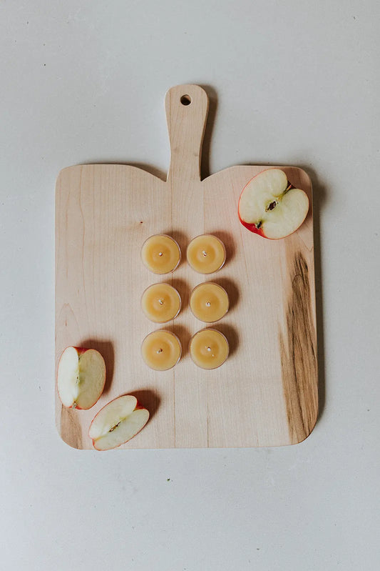 Top-down view of eight tea lights in rows on a wooden cutting board with apple slices.