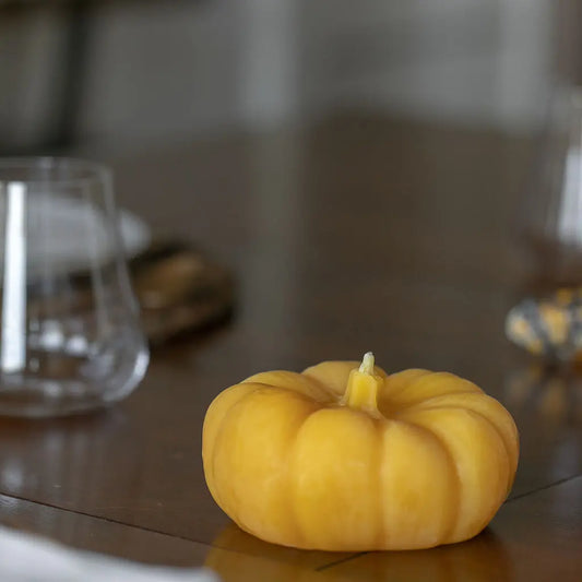 Unlit chubby pumpkin candle with a carved stem on a dark wood table near a glass.