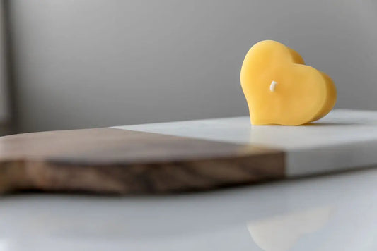 Golden heart-shaped candle standing upright on a wood and marble board.