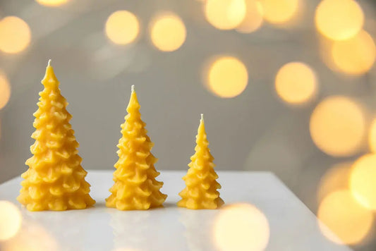Three tiered tree candles in small, medium and large on a white table with warm bokeh lights.