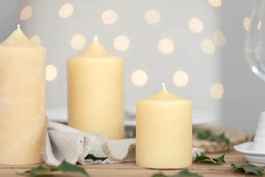 Three bell-top beeswax pillars in different heights on a table with soft lights; shared candle photo.