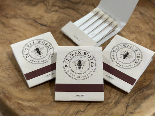 Three closed white bee-logo matchbooks in front of an open book of matches on a wood table.