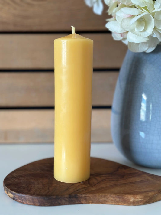 Close view of a tall narrow pillar candle on olive wood beside a blue vase of hydrangeas.