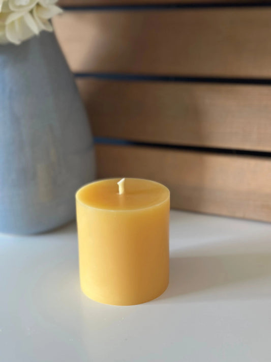 Flat-top short pillar candle on a white surface in front of a blue vase and wood slat wall.