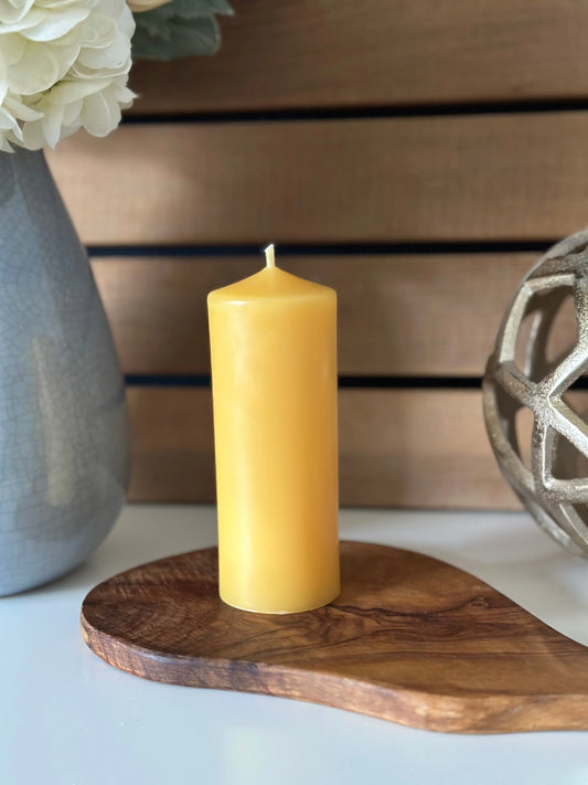 Narrow pillar candle on olive wood between a grey vase and an openwork metal sphere.