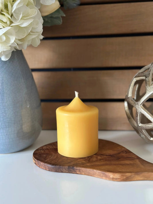 Bell-top pillar candle on an olive wood board between a blue vase and a metal sphere.