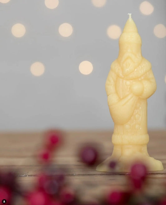 Close view of a pale Victorian Santa candle on wood with soft lights and red berries.