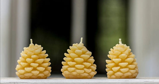 Three pine cone candles in a row on a white ledge in front of a dark window.