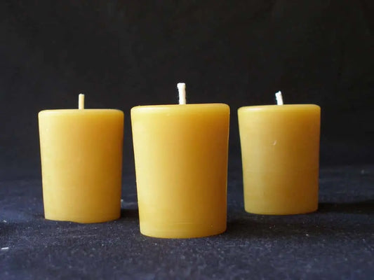Three yellow beeswax votive candles with white wicks standing in a row on dark fabric.