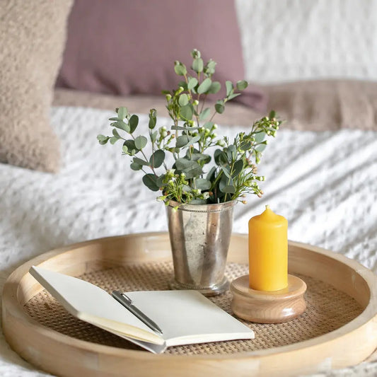 Short narrow pillar on a wood base in a rattan tray with an open notebook and greenery.