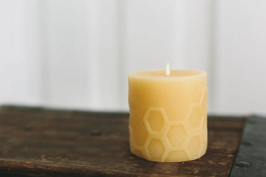 Close view of a short, pale honey honeycomb pillar candle on a rustic wooden board.